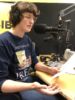 Femme qui tient une feuille de papier et qui parle à un micro dans le cadre d'un enregistrement radio.