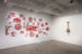 Photo of an exhibition view of "Setting the Table". The white wall on the left is occupied by Karen Tam's Chef Lee's Wok'n'Roll Garden (2004-2010), a wall installation consisting of a series of "Chinese" symbols cut from red paper. The symbols are a clichéd Western creation of Chinese restaurants. The white wall to the right of the photo is occupied by Pierre Ayot's mural 'La cuisine de Bocuse' (1986). Less imposing, but just as colourful, it contrasts with the empty space surrounding it.