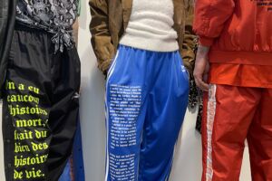 Colour photograph showing the bodies of three people wearing clothing inspired by the 1980s and 1990s, on which quotations have been printed in connection with the AIDS/HIV crisis.