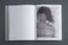 Black and white photograph of an open book on a dark grey background. The left page is blank, the right page features the blurred upper body of a person with their head turned to the side. It is a photo-based gel transfer on archival paper.