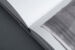 Black and white photograph of a close-up of a book corner. The left page is blank, the right page shows the printed corner of an artwork, which appears to lift from the printed paper.